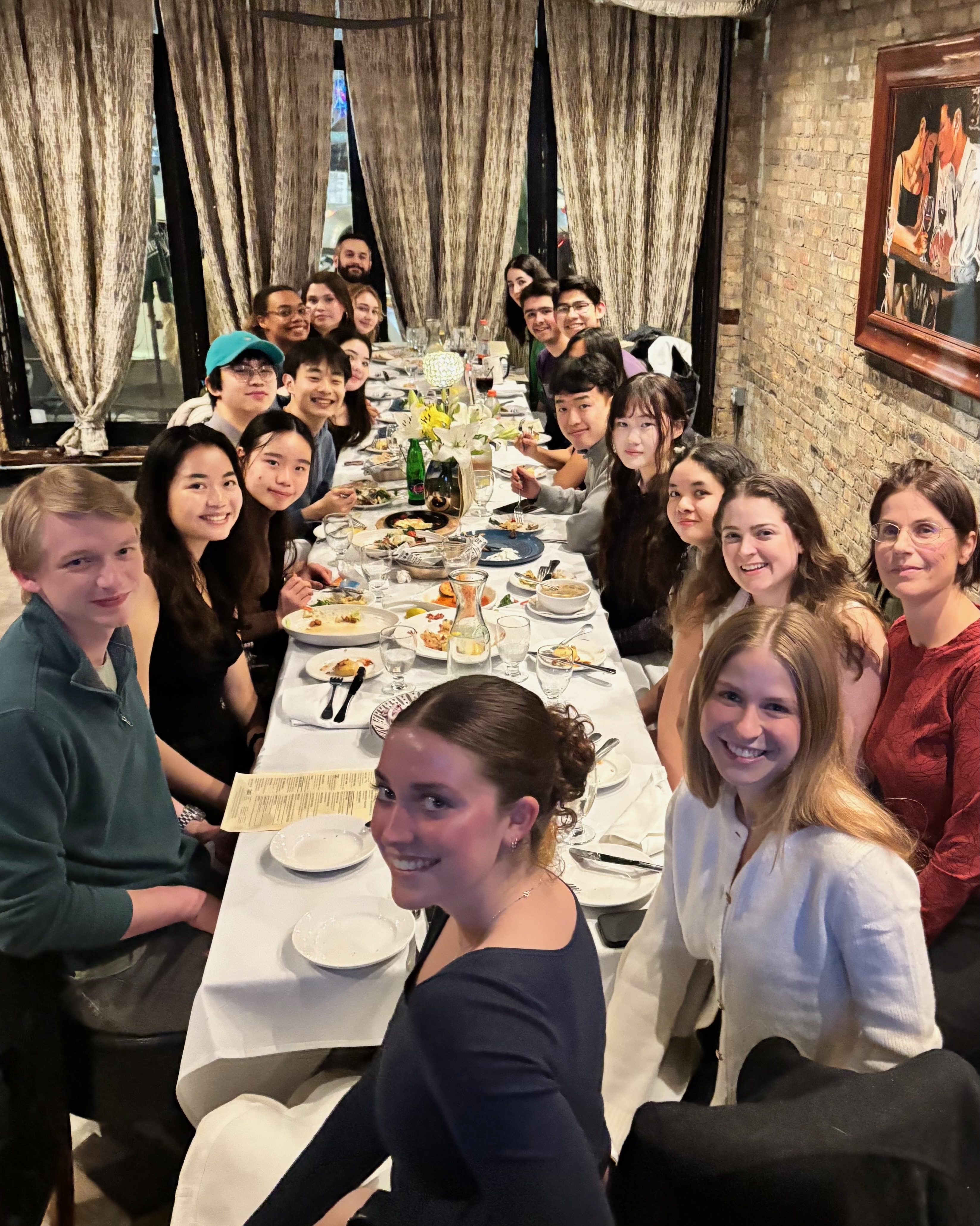 Smiling students and professor sit around a long dining table at a restaurant