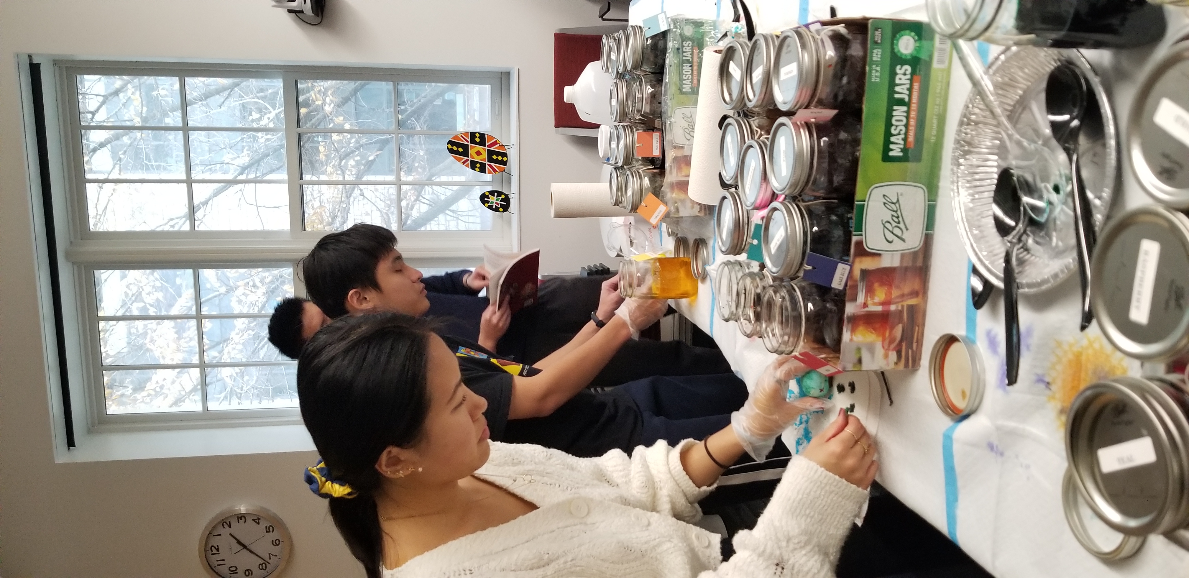 students dip their eggs into glass jars of colored dyes