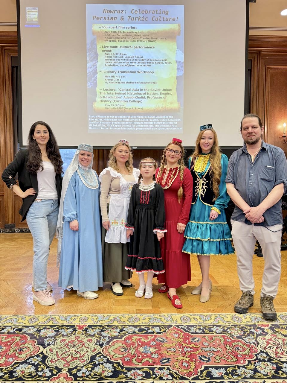 A small group of women dressed in traditional Tatar cultural attire are flanked by graduate student organizers Bita Takrimi and Adam Willson